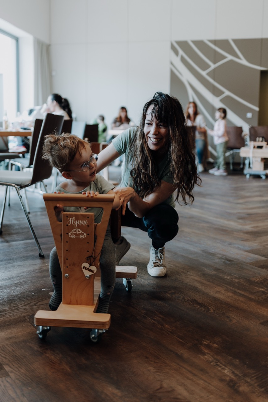 Eine junge Frau mit ihrem Kind, welche zusammen sehr viel Spaß haben. Das Kind sitzt auf einem Holzwägelchen.