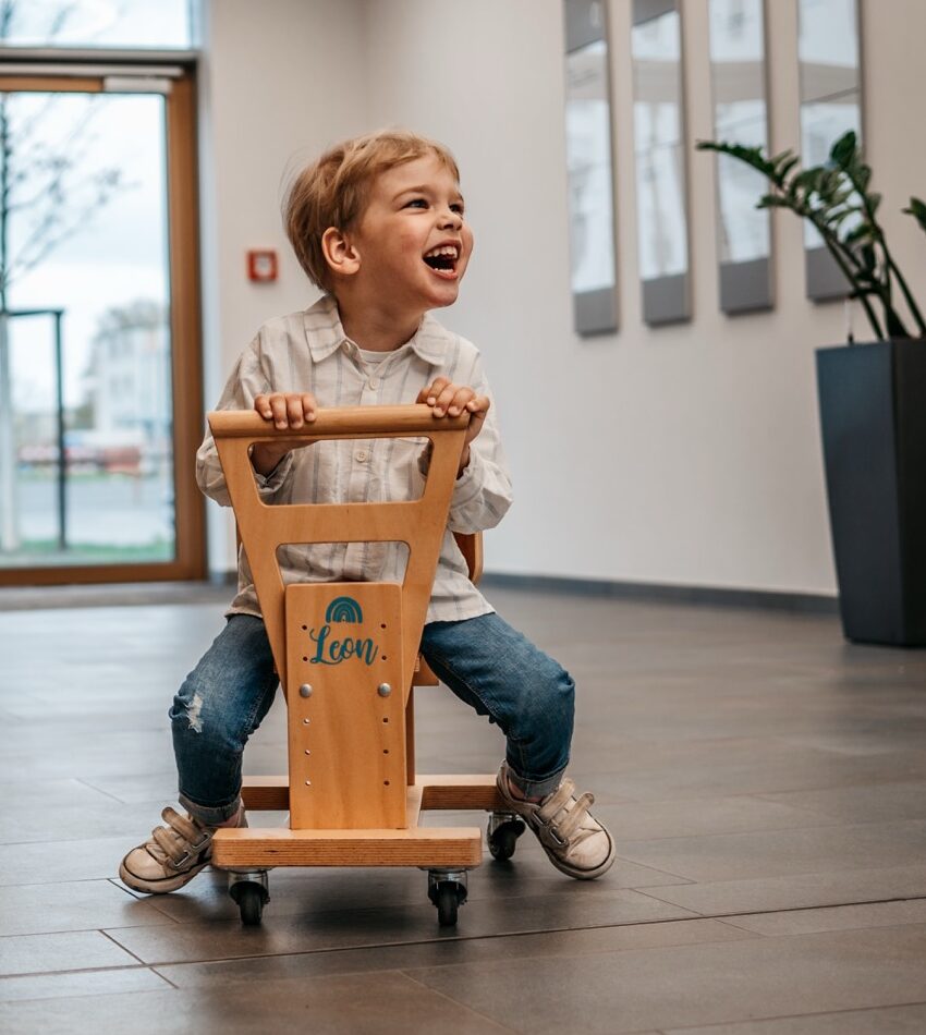 Leon freut sich und sitzt auf seinem Holzwägelchen.
