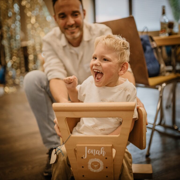 Mann mit seinem Kind, dass auf einem Holzwägelchen sitzt.