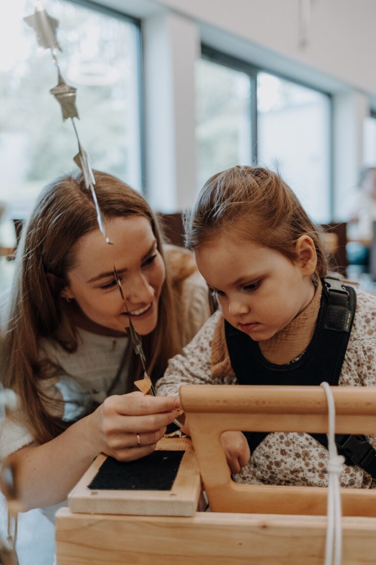 Eine Frau mit ihrem Kind. Das Kind sitzt auf dem Holzwägelchen.