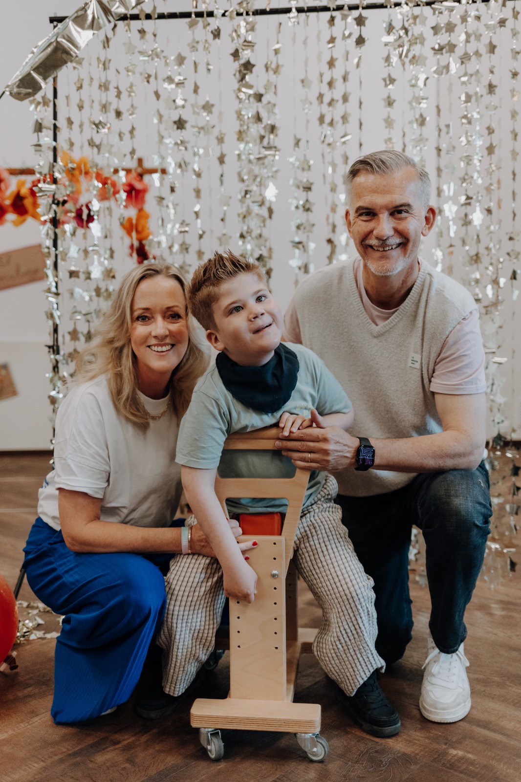 Ein Familienbild von Eltern mit ihrem Kind, welches auf dem Holzwägelchen sitzt.