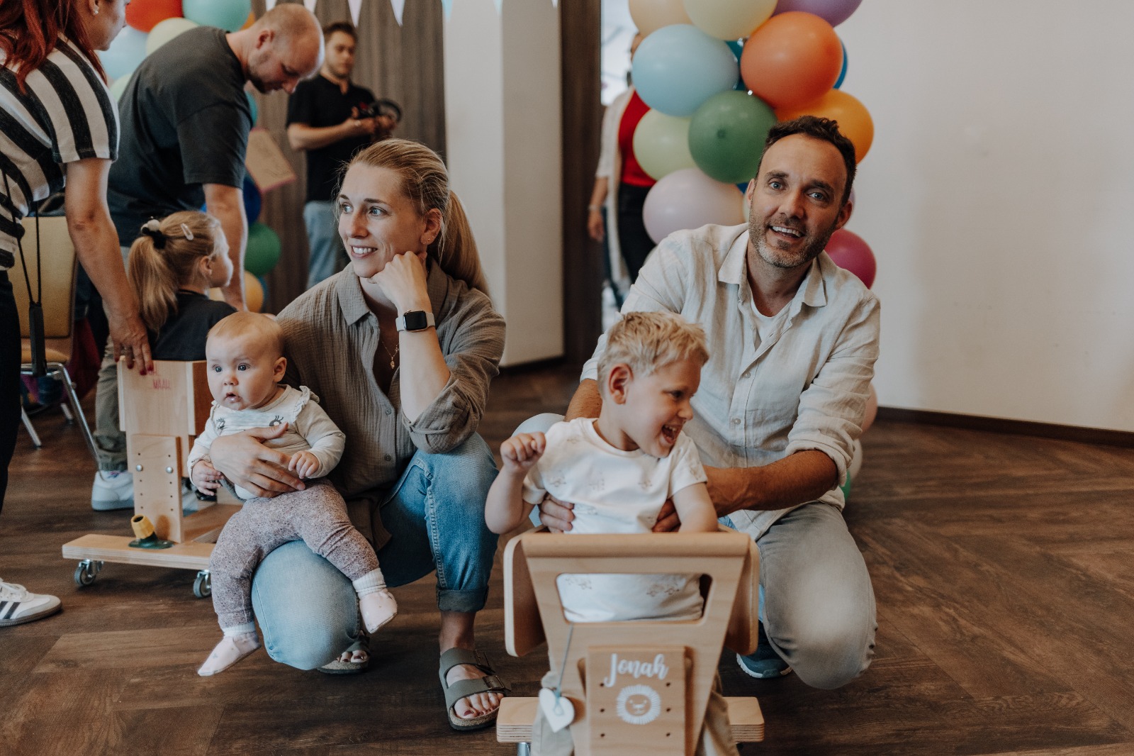 Eine Familie mit ihren zwei Kindern. Ein Kind hat leider eine Behinderung und benötigt das Holzwägelchen