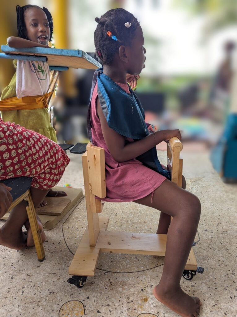 Mädchen sitzt auf dem Holzwägelchen und hat ihre Büchertasche auf